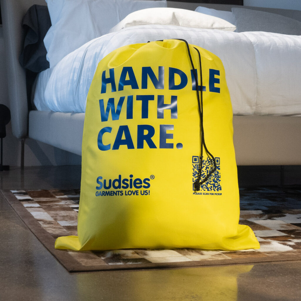 Yellow Sudsies laundry bag placed beside bed ready for pickup and delivery service