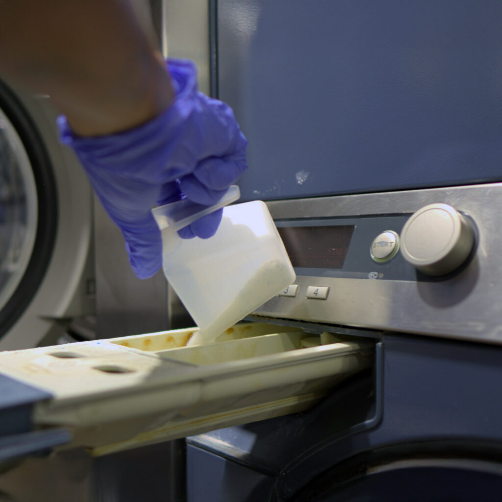 Sudsies team member adding detergent to commercial washer during garment care process